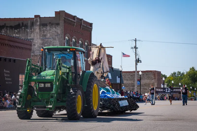 A green tractor pulls a float of a robed figure above sculpted waves.